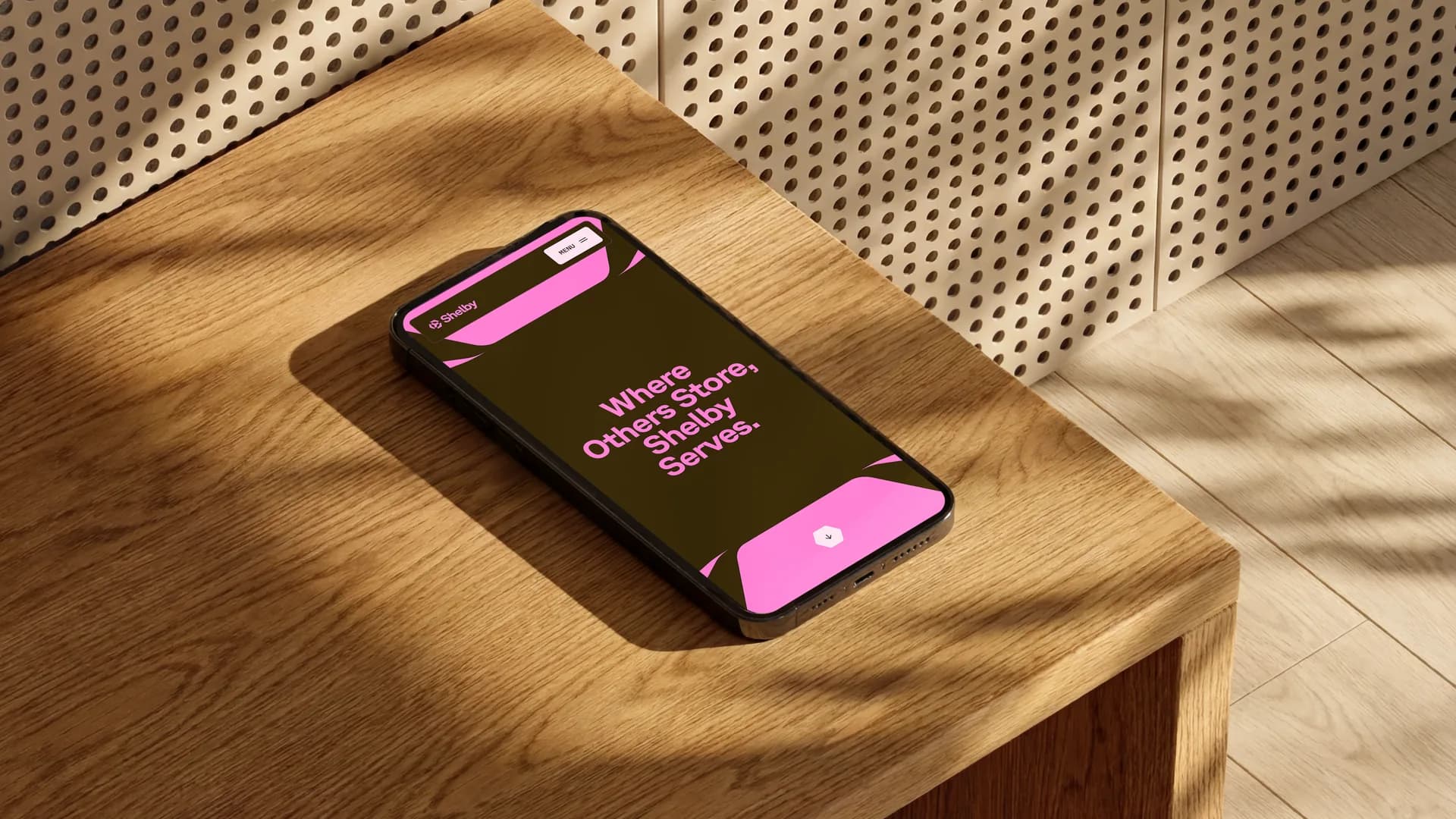 Shelby website on a phone on a wooden desk beneath a perforated wall