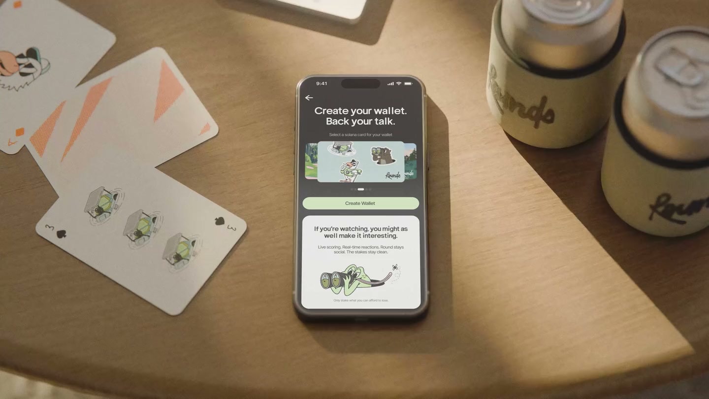 Rounds app on a phone on a sunlit wooden table beside branded cans and printed cards
