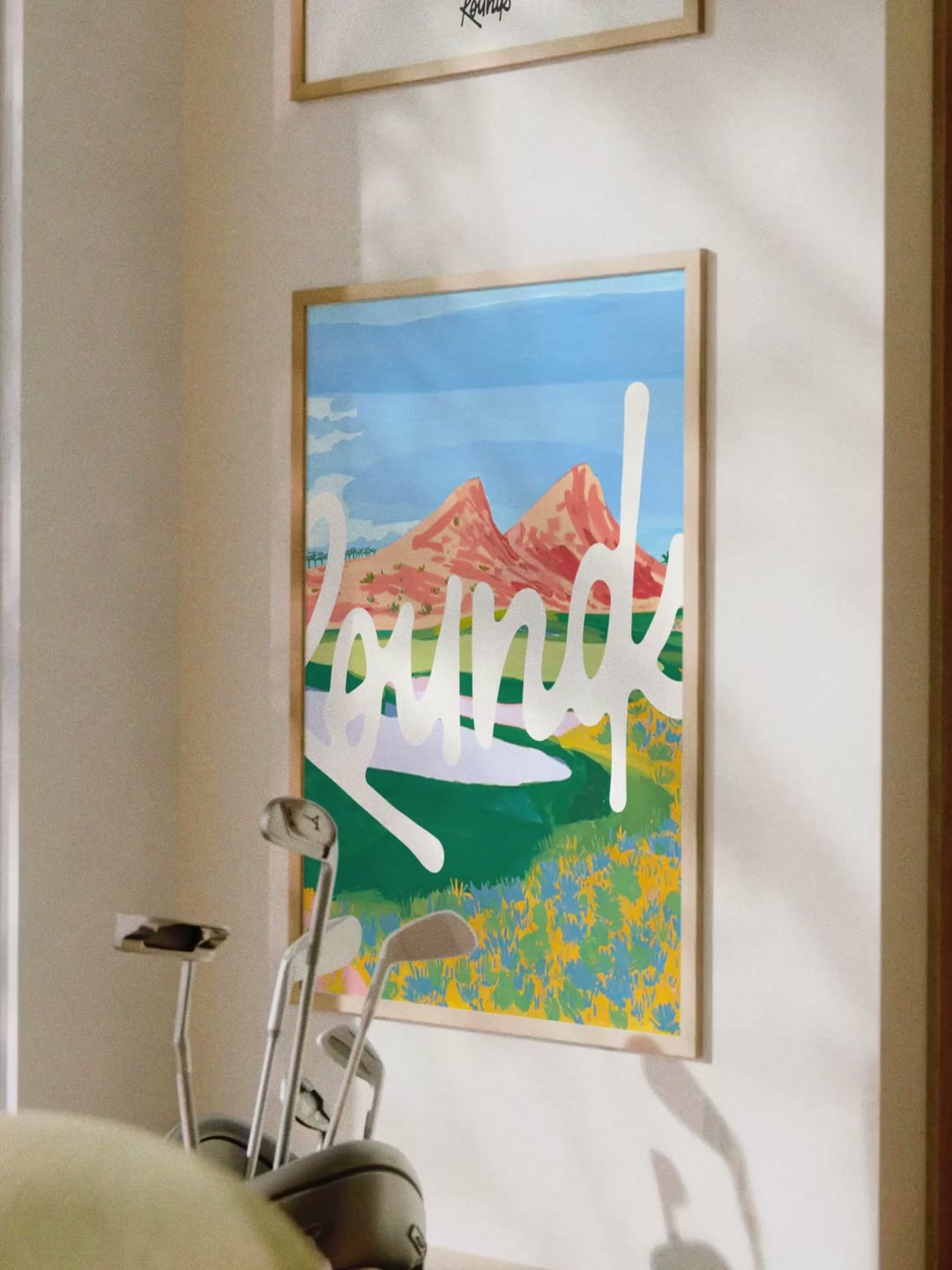 Colourful Rounds poster in the clubhouse beside golf clubs and a window onto the course